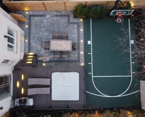 Image depicts an interlocking patio in a backyard with a basketball court.