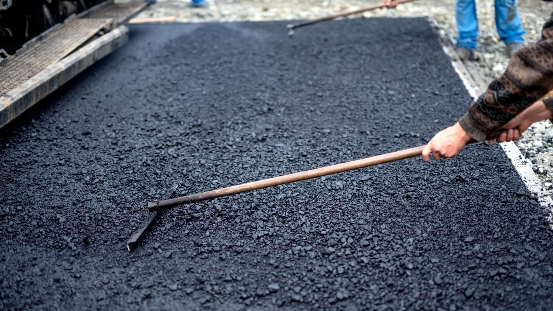 Worker leveling fresh asphalt on a road